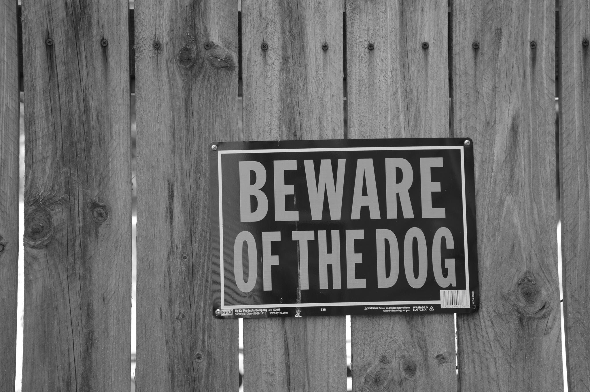 a weather worn wooden fence with a sign on it that says "Beware of the dog" in all capital letters