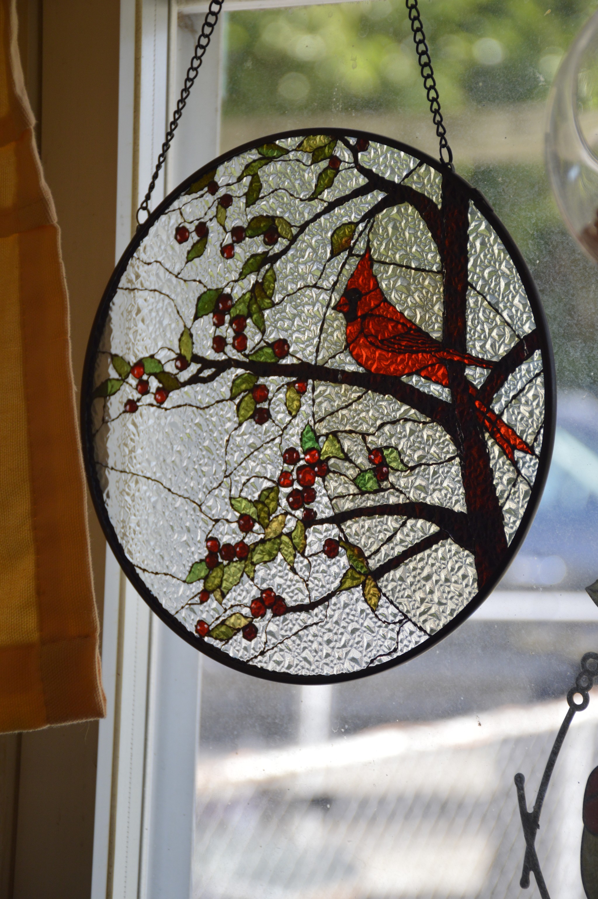 a glass art piece of a male cardinal sitting on a branch that is growing leaves and berries